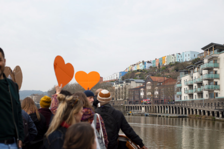 Orange hearts being held up with Bristol Harbourside in the background