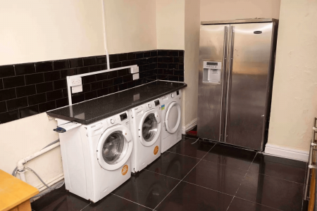 A picture of a room with a fridge, dryer, and wash.